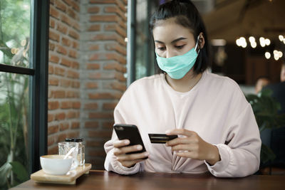 Young woman using smart phone on table at window