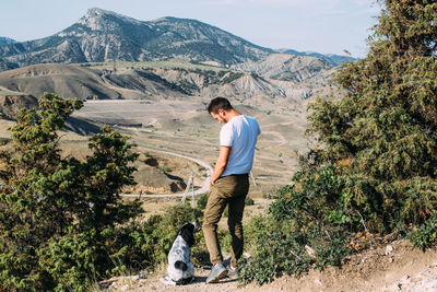 Male owner of spaniel dog walking against mountains background.