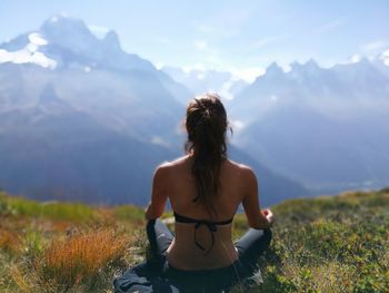 Rear view of woman meditating while sitting on grassy field against sky