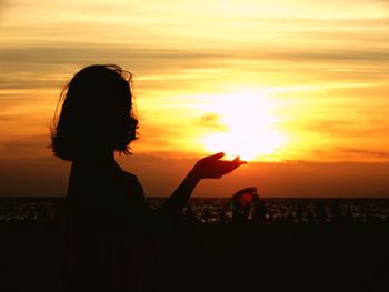 Optical illusion of woman holding sun at beach during sunset