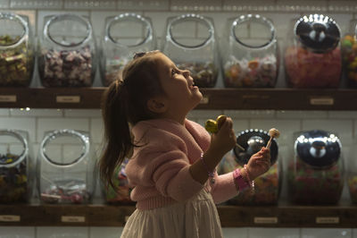 Side view of happy girl holding candies while standing in shop