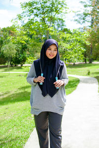 Picture of a young muslim woman outside a green nature park doing exercises with a skipping rope.