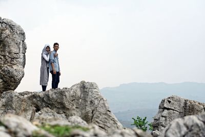 Couple standing on cliff against sky