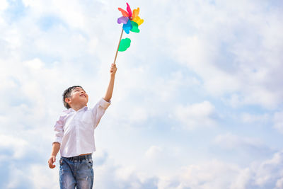 Low angle view of boy holding pinwheel toy against sky