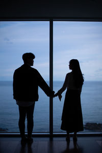 Rear view of silhouette couple standing against sky during sunset