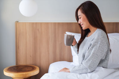 Young woman using phone while sitting on bed at home