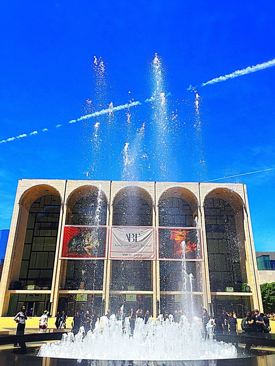 blue, building exterior, architecture, built structure, low angle view, sky, motion, outdoors, day, fountain, leisure activity, clear sky, arts culture and entertainment, spraying, incidental people, lifestyles, men, city, enjoyment