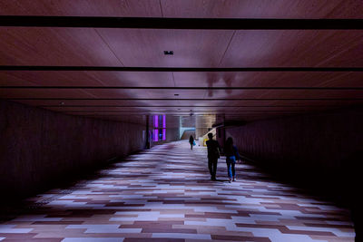 Rear view of people walking on footpath in tunnel