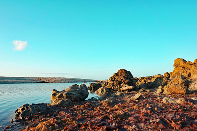 Rocks in sea against clear blue sky