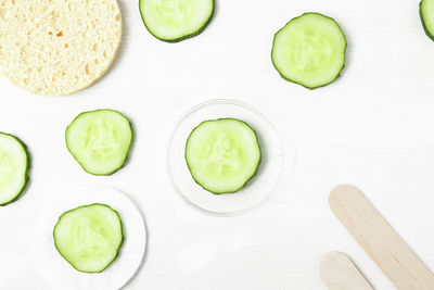 Pieces of fresh green cucumber on a white background with accessories, sponge and spatulas 