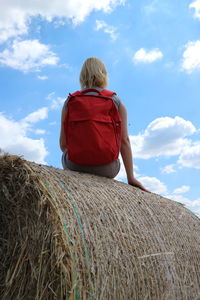 Rear view of backpack woman sitting on hay bale