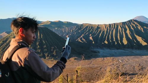 Young man photographing against volcanic mountains