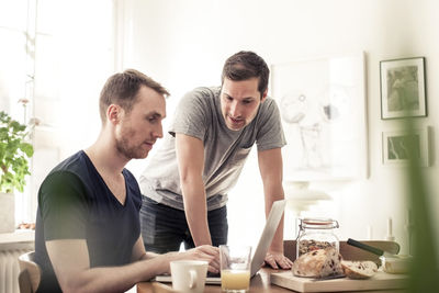 Young homosexual couple using laptop together at breakfast table in home