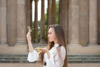 Close-up of young woman holding flower standing against columns