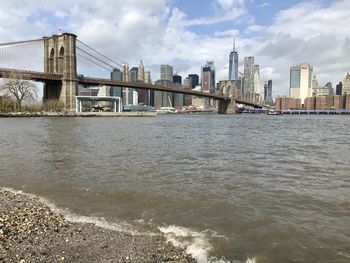 Bridge over river by buildings in city against sky