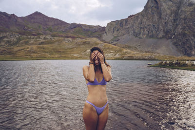 Woman wearing bikini hiding face while standing in lake at ibones of anayet