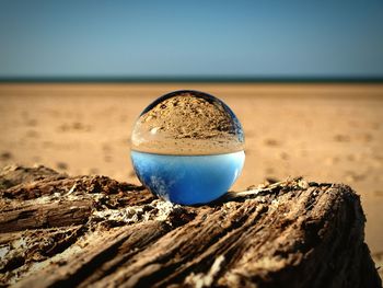 Close-up of drink on sand against clear blue sky