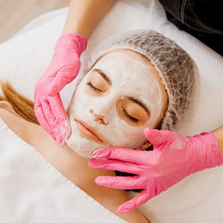 Hands of beautician applying cream on woman's face