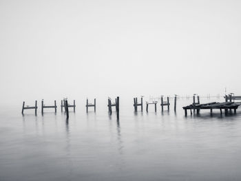 Wooden posts in sea against clear sky