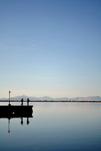 Silhouette man on lake against clear blue sky