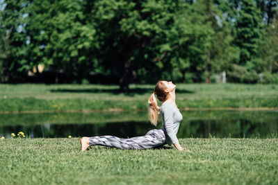 Full length of young woman exercising by pond on field