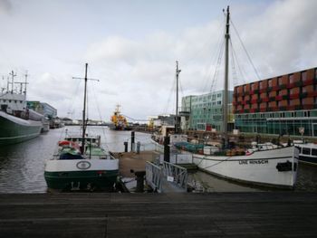 Boats moored at harbor in city against sky