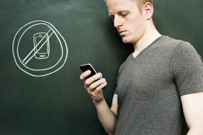 Close-up of man using phone with drawing on blackboard