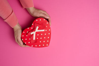 Two female hands hold a red heart-shaped box on a pink background. festive backdrop