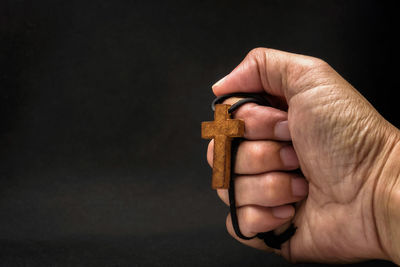Close-up of hand holding cross against black background