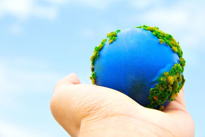 Close-up of hand holding globe against blue sky