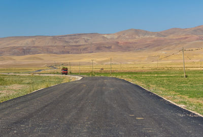 Road amidst field against clear sky