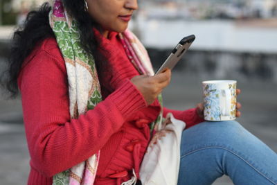 Midsection of woman having coffee while using mobile phone outdoors