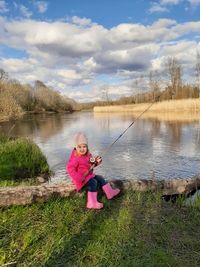 Portrait of a girl sitting on lake against sky