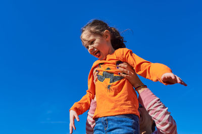 Pretty girl being held up in the air by mom against a blue sky