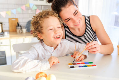 Mother and boy holding paintbrush sitting at home