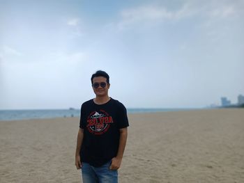 Portrait of young man standing at beach against sky