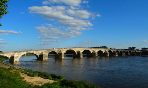 Arch bridge over river against blue sky