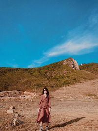 Woman with arms raised on mountain against blue sky