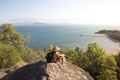 Woman sitting on rock by sea against sky