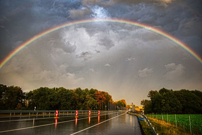 Rainbow over wet road against sky during rainy season