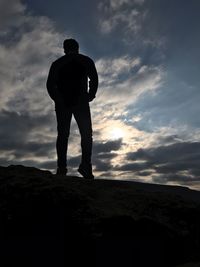 Rear view of silhouette man standing on rock against sky