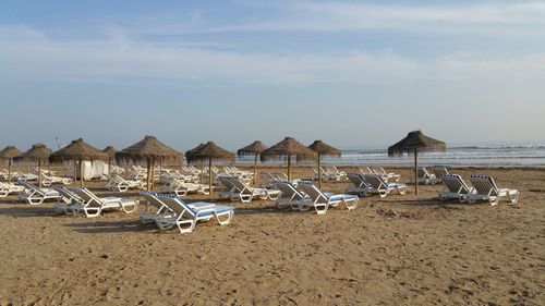 Deck chairs on beach against sky