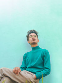 Thoughtful young man sitting against wall