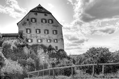 Low angle view of old building by trees against sky in monochrome