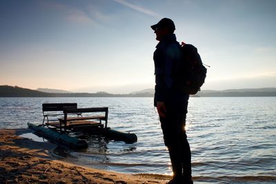 Tall tourist with backpack walk on beach at abandoned pedal boat in sunset. autumn sunny day at sea