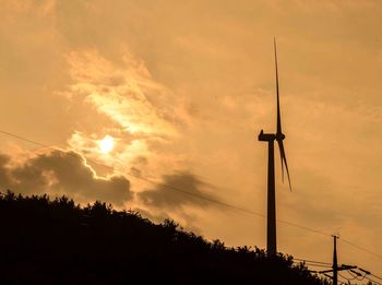 Low angle view of silhouette wind turbine and plants against cloudy sky during sunset