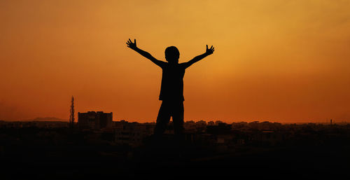 Silhouette man with arms outstretched against sky during sunset