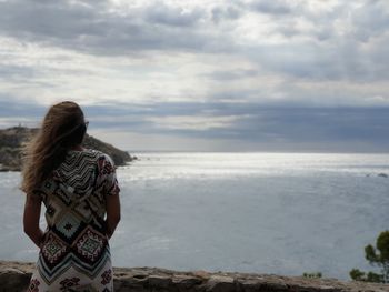 Rear view of woman standing by sea against sky