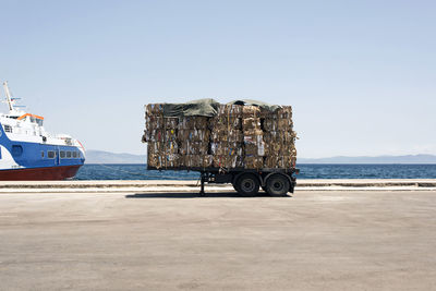 Cardboards on cart by ship in sea against sky