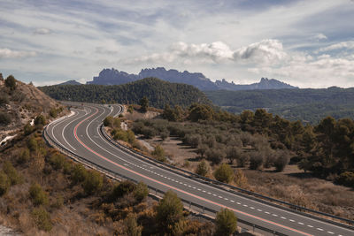 Curved road and montserrat mountain in the background in a landscape under a cloudy sky in catalonia